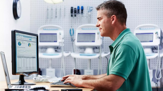 A biomed reads information on a computer screen. Tools and Connex® Vital Signs Monitors are in the background