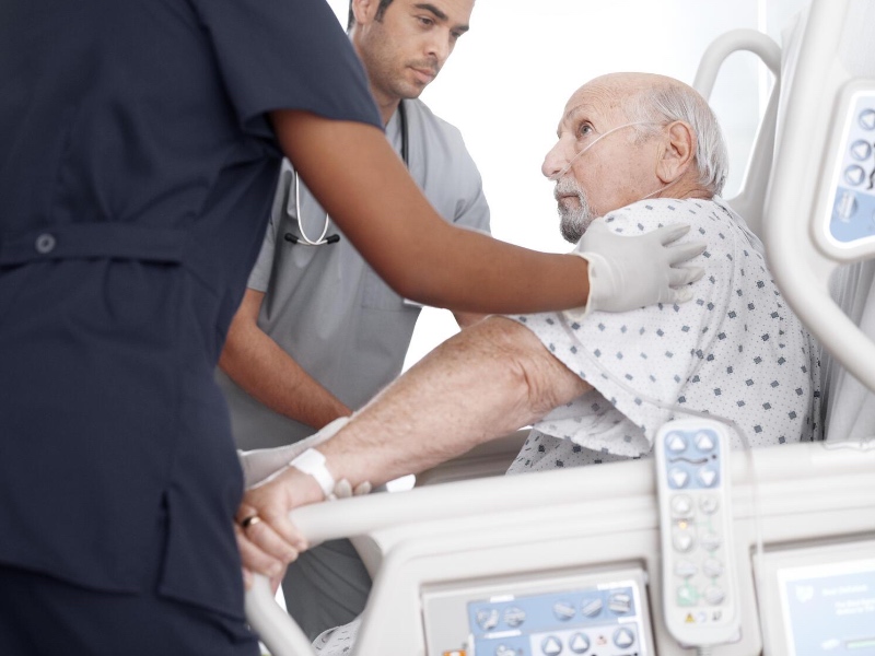 An older patient being assisted by hospital staff in a Progressa bed.